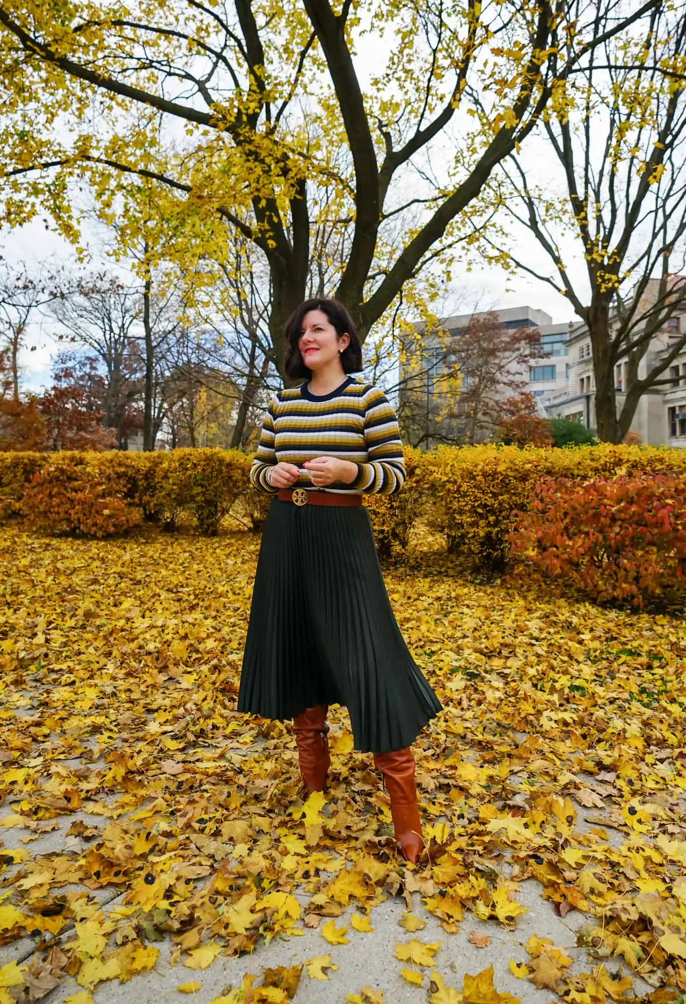 A women wearing a green pleated skirt, striped sweater and brown