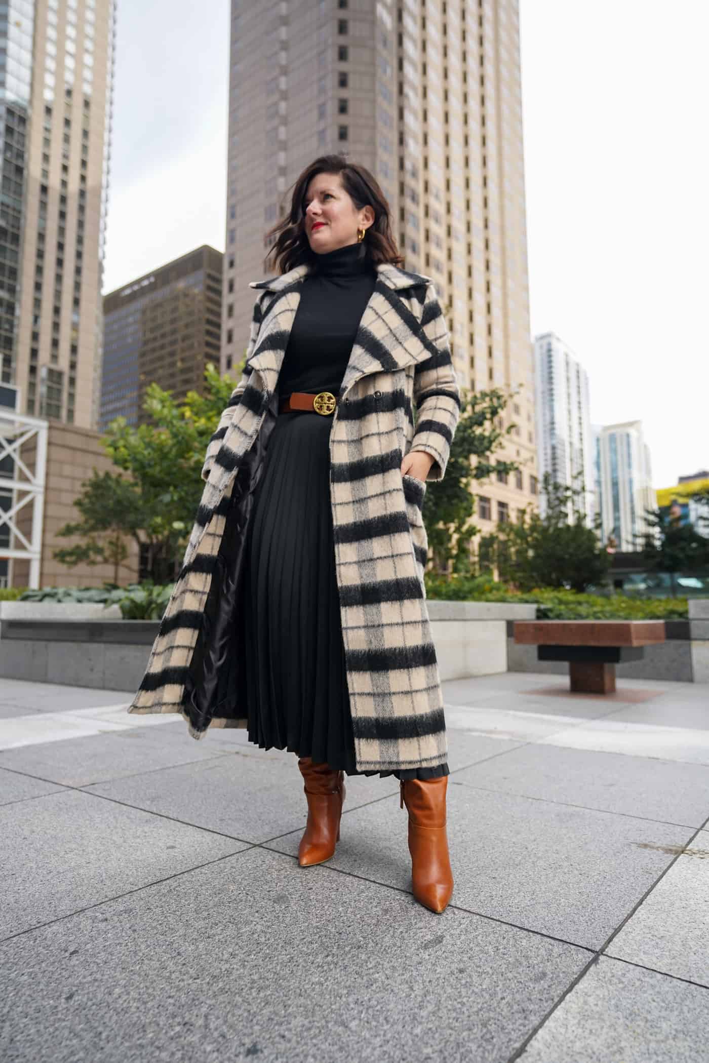 A Lily Love Affair shares how to wear a pleated skirt with black sweater, long plaid coat and brown boots