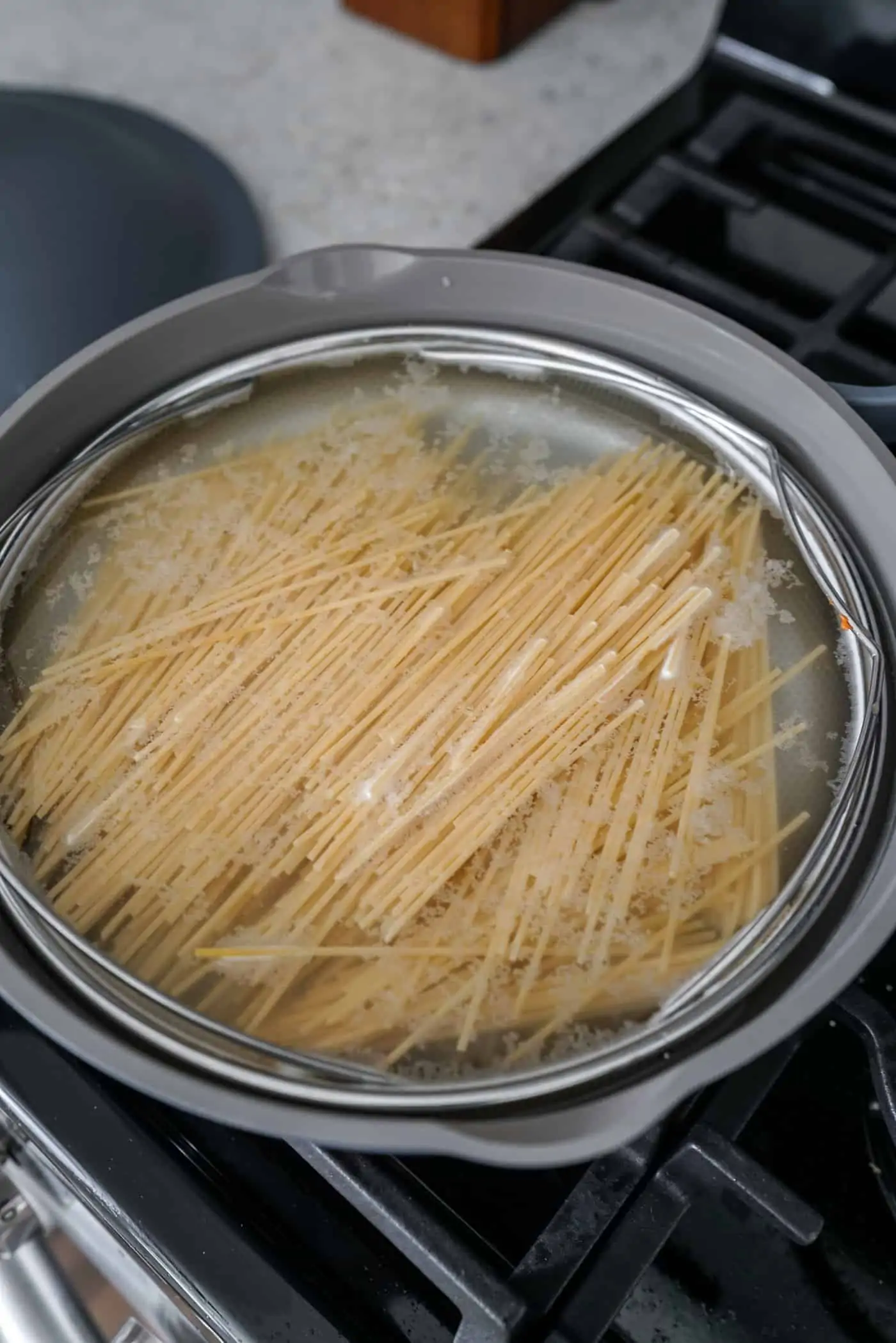 An Our Place Always Pan filled with cooking spaghetti pasta shells. 
