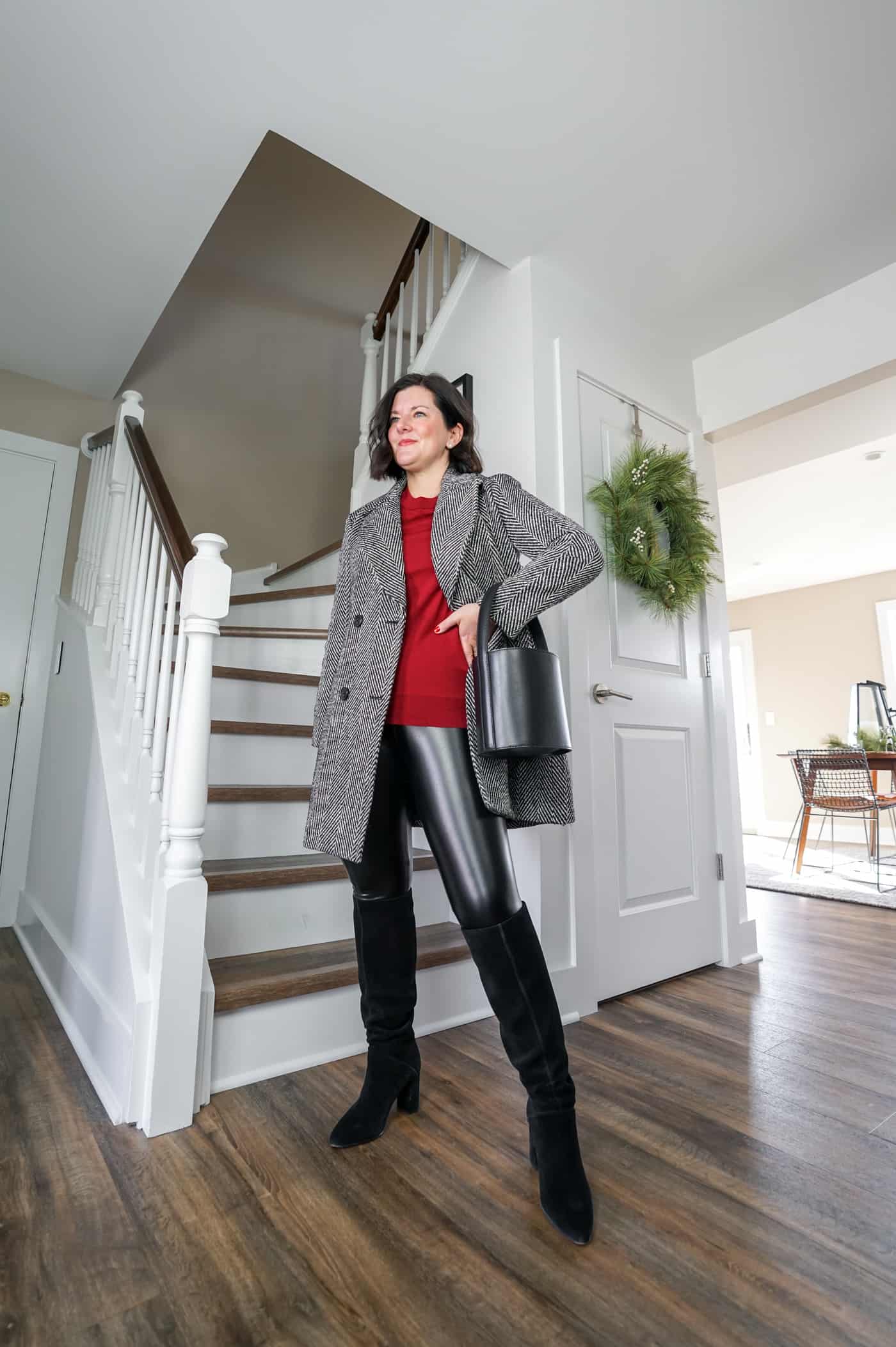 A petite women wearing faux leather leggings with black knee high suede boots and a black and white coat 